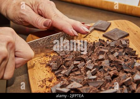 Chef cuts bitter chocolate into pieces on wooden board in the kitchen Stock Photo