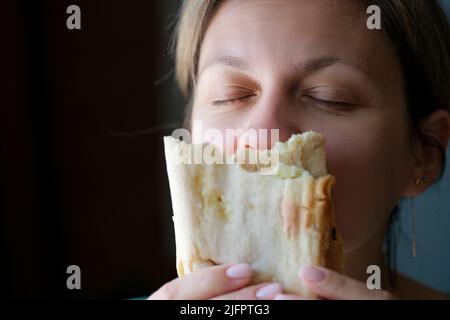 Young woman closing eyes in pleasure and eating tasty shawarma Stock Photo