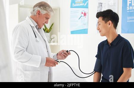 Theres a tool for every test. Shot of a mature doctor monitoring a patients blood pressure at a hospital. Stock Photo