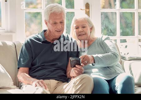 How does this work. Cropped shot of an affectionate senior couple sitting in their living room at home. Stock Photo