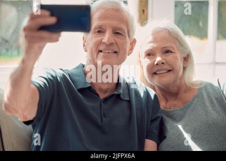 A selfie for the kids. Cropped shot of an affectionate senior couple sitting in their living room at home. Stock Photo