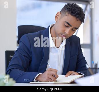Ill jot that idea down for next time. Shot of a young businessman writing notes while working in an office. Stock Photo