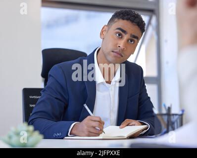 Taking note of all feasible ideas. Shot of a young businessman writing notes while working in an office. Stock Photo