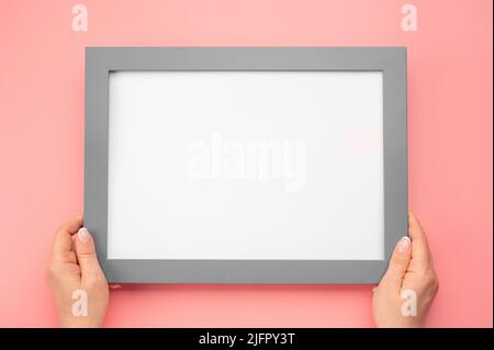 Holding frame mockup. Photo Mockup. Woman hands hold gray frame. For frames and posters design. Frame size A4. on pink background. blank photo frame b Stock Photo