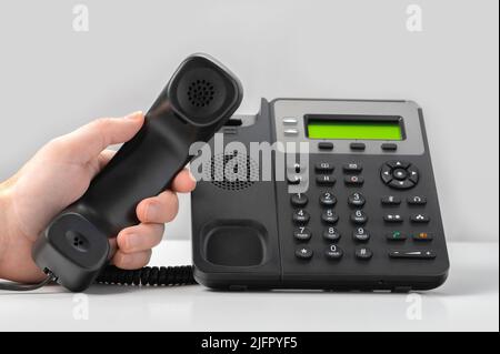 hand holding voip telephone receiver on gray background. Dialing telephone keypad concept for communication, contact us and customer service support. Stock Photo