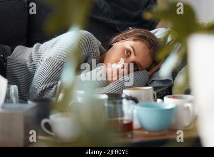 Days like this are the worst. Shot of a young woman lying on her couch blowing her nose and looking depressed. Stock Photo