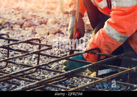 Builder's hands fixing steel reinforcement bars at construction site. Steel fixer assembling reinforcement cage. Selective focus Stock Photo