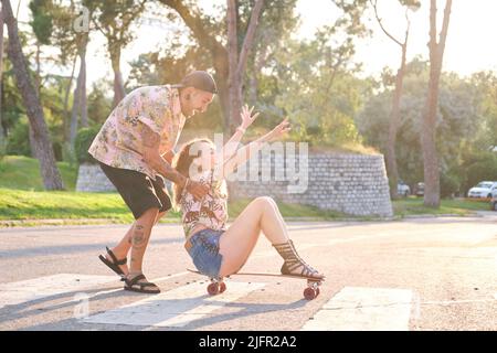 Young cool tattooed couple having fun skateboarding. Stock Photo