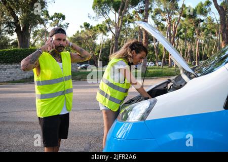 Young tattooed couple in reflective safety vest calling for road assistance.