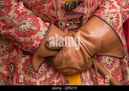 Man hands are gloved and an ornate vintage robe with retro weapons behind an old belt. Male hands in antique clothes with a cane Stock Photo