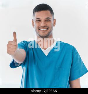 Here to keep my community in good health. Portrait of a young doctor showing thumbs up in a hospital. Stock Photo