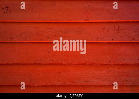 Close-up of an exterior wood wall painted red. Horizontal planks of rustic wood with knots and thin cracks. Rough texture photo background. Copy space Stock Photo