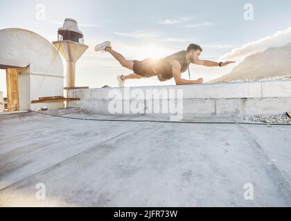 Ive made some adjustments to my workout routine. Shot of a man doing a single-arm plank while on a rooftop. Stock Photo