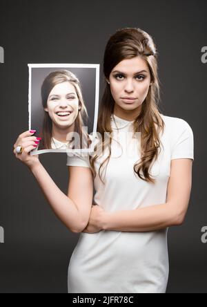 Different day, different mood. Studio shot of an attractive young woman dressed up in 60s wear and holding a photograph of herself smiling against a Stock Photo