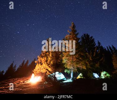 Campground with touristic equipment during night time with starry sky and bonfire, concept of hiking vacations with tourist tents for recreating and resting in the mountains. Stock Photo