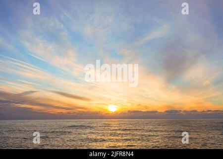 Sunset over the water surface of the sea horizon and cirrus clouds Stock Photo
