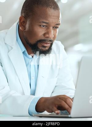 Where are the reports. Shot of a handsome mature scientist sitting alone in his laboratory and using his laptop. Stock Photo