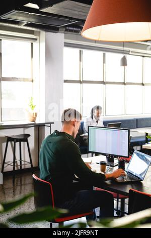 Young caucasian businessman using computer and laptop at desk in creative office Stock Photo