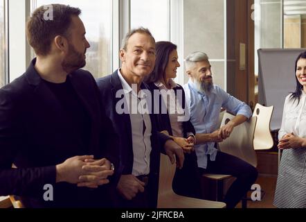 Senior businessman standing surrounded by his colleagues who are talking in coworking center. Stock Photo