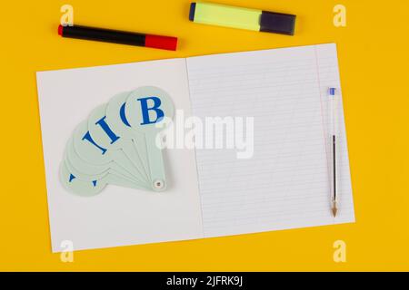 School notebook on a yellow background with copy space for text, colorful markers, English alphabet. Back to school. Blank sheet of paper with oblique Stock Photo