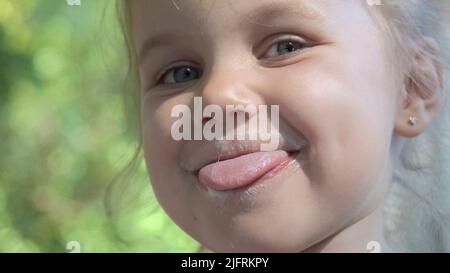 Portrait of cute little girl sticking her tongue out and smiling after eating delicious ice cream. Extreme close-up portrait of little girl. Stock Photo