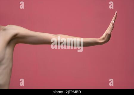Young woman's stretched skinny arm and fist . Isolated on blue background.  Stock Photo