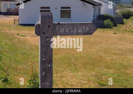 A public footpath sign stands in front of holiday chalet close to a sunny bay at Blue Anchor in Somerset. Stock Photo