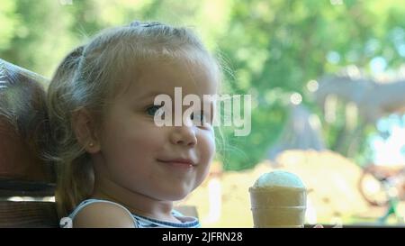 Odessa, Ukraine, Eastern Europe. 4th July, 2022. Cute little girl eats ice cream outside. Close-up portrait of blonde girl sitting on park bench and eating icecream. (Credit Image: © Andrey Nekrasov/ZUMA Press Wire) Stock Photo