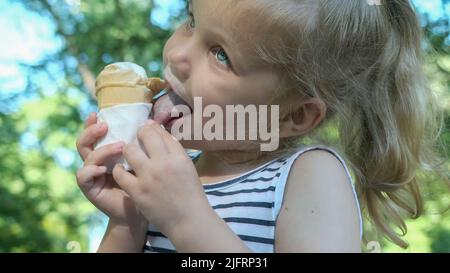 Odessa, Ukraine, Eastern Europe. 4th July, 2022. Cute little girl eats ice cream outside. Close-up portrait of blonde girl sitting on park bench and eating icecream. (Credit Image: © Andrey Nekrasov/ZUMA Press Wire) Stock Photo