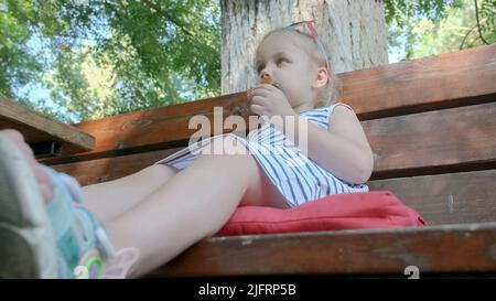 Odessa, Ukraine, Eastern Europe. 4th July, 2022. Little girl eats gingerbread. Close-up portrait of blonde girl sitting on park bench and eating cookies. (Credit Image: © Andrey Nekrasov/ZUMA Press Wire) Stock Photo