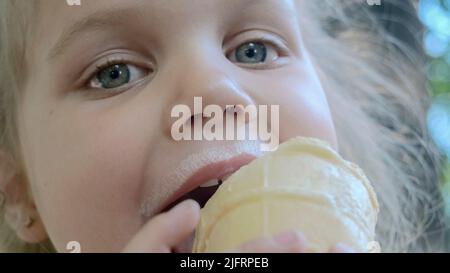 Odessa, Ukraine, Eastern Europe. 4th July, 2022. Cute little girl eats ice cream outside. Close-up portrait of blonde girl sitting on park bench and eating icecream. (Credit Image: © Andrey Nekrasov/ZUMA Press Wire) Stock Photo