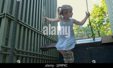 Odessa, Ukraine, Eastern Europe. 4th July, 2022. Smiles little rides on swing. Close-up of a blonde girl is swinging on swing in city park. (Credit Image: © Andrey Nekrasov/ZUMA Press Wire) Stock Photo