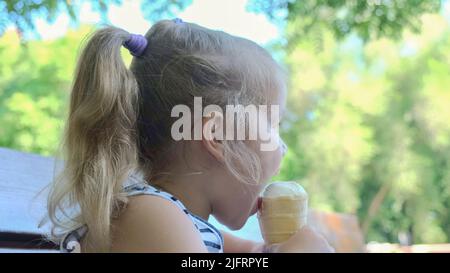 Odessa, Ukraine, Eastern Europe. 4th July, 2022. Cute little girl eats ice cream outside. Close-up portrait of blonde girl sitting on park bench and eating icecream. (Credit Image: © Andrey Nekrasov/ZUMA Press Wire) Stock Photo