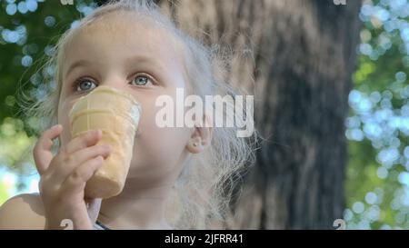 Odessa, Ukraine, Eastern Europe. 4th July, 2022. Cute little girl eats ice cream outside. Close-up portrait of blonde girl sitting on park bench and eating icecream. (Credit Image: © Andrey Nekrasov/ZUMA Press Wire) Stock Photo