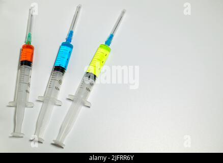 Three medical syringes with the vaccines of different colors on white background. Vaccine against corona virus and monkeypox. Space for text. Stock Photo