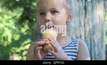 Odessa, Ukraine, Eastern Europe. 4th July, 2022. Cute little girl eats ice cream outside. Close-up portrait of blonde girl sitting on park bench and eating icecream. (Credit Image: © Andrey Nekrasov/ZUMA Press Wire) Stock Photo