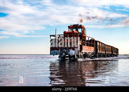 The train floats on the water against the blue sky. Salt industry, salt mining. Stock Photo