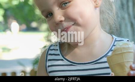 Odessa, Ukraine, Eastern Europe. 4th July, 2022. Cute little girl eats ice cream outside. Close-up portrait of blonde girl sitting on park bench and eating icecream. (Credit Image: © Andrey Nekrasov/ZUMA Press Wire) Stock Photo