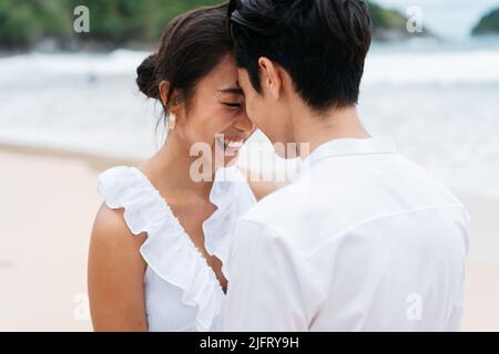 Happy smiling Asian 30s couple in relationship head to head on the beach in summer. A romantic couple wearing a white shirt and dress Stock Photo
