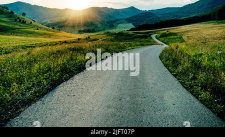 Road to the mountains through a field. road goes into the distance to the sunset or dawn. Stock Photo