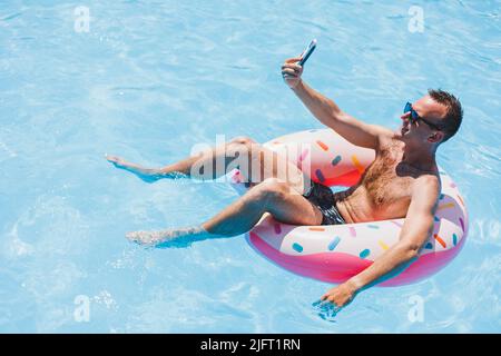 An attractive man is relaxing on an inflatable ring in the pool. A man in the pool is talking on the phone. vacation and free time concept Stock Photo