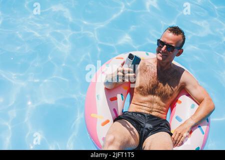 An attractive man is relaxing on an inflatable ring in the pool. A man in the pool is talking on the phone. vacation and free time concept Stock Photo