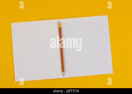 School notebook on a yellow background with copy space for text and pencil. Back to school. Blank sheet of paper with oblique lines in exercise book. Stock Photo