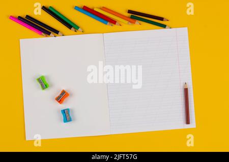 School notebook on a yellow background with copy space text, colorful pencils, pencil sharpeners. Back to school. Blank sheet of paper with oblique Stock Photo