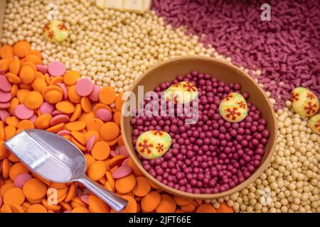Ruby chocolate dragee in bowl of chocolate on background of colored chocolate drops. Stock Photo