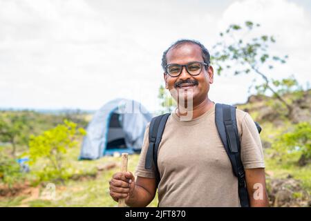 Portrait of happy smiling traveller with hiking stick in front of camping tent looking at camera - concept of hobby,vacation and holidays. Stock Photo