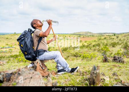 Thirsty man drinking water while sitting on top of hill during trekking - concept of taking break, healthy active lifestyle and hobby. Stock Photo