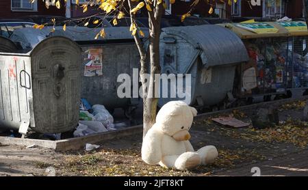Kyiv, Ukraine March 11, 2022: A large teddy bear thrown into the garbage sitting near a dumpster Stock Photo