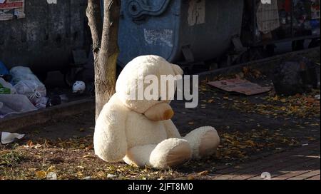 Kyiv, Ukraine March 11, 2022: A large teddy bear thrown into the garbage sitting near a dumpster Stock Photo