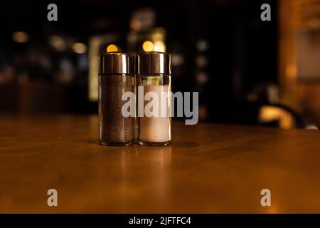 Salt and pepper shakers standing on a wooden table in a dark bar Stock Photo